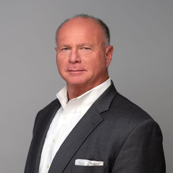 A man in a suit and tie standing up against a gray background.